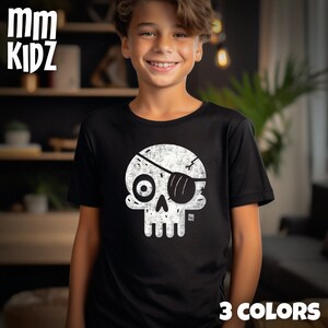 Op de afbeelding: Zwart T-shirt met een witte schedelafbeelding met een ooglapje. Het shirt heeft de tekst "mm KIDZ" in het wit linksboven en "3 COLORS" rechtsonder. Het ontwerp is in een distressed stijl.