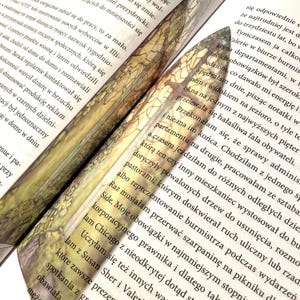 May include: Close-up of a book with a bookmark featuring a stained glass design. The bookmark is shaped like a sword and has a colorful, intricate pattern.