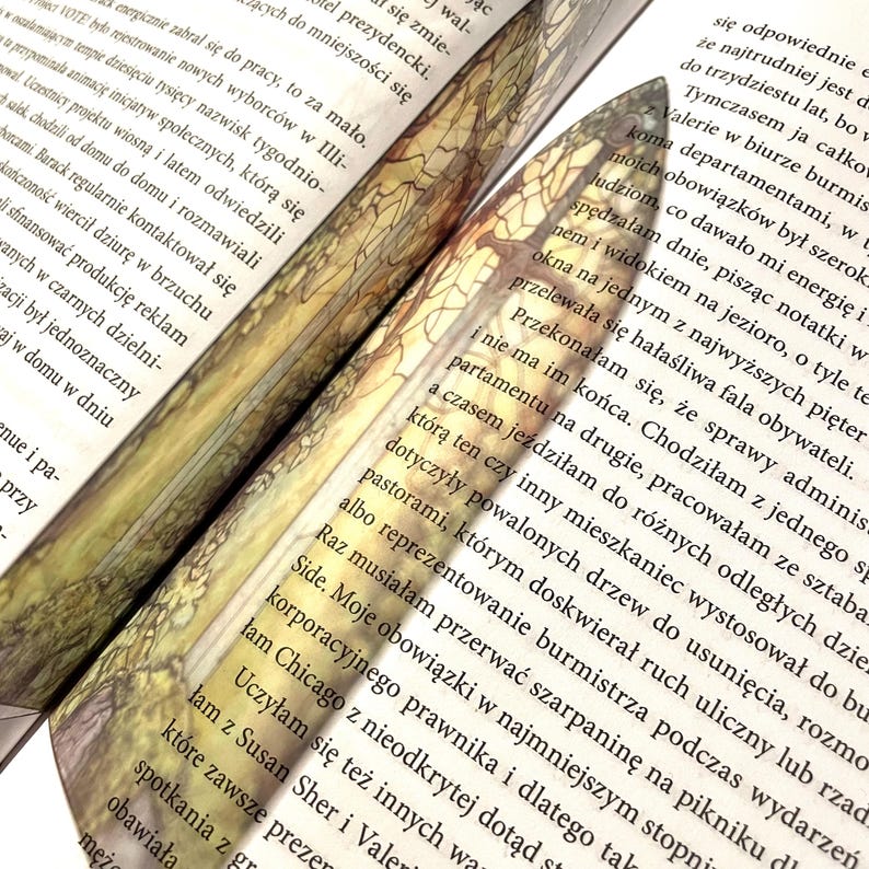 May include: Close-up of a book with a bookmark featuring a stained glass design. The bookmark is shaped like a sword and has a colorful, intricate pattern.