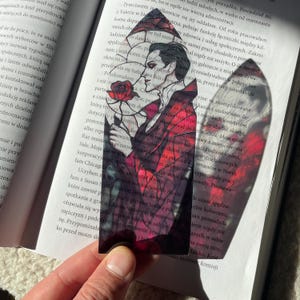 May include: A stained glass bookmark depicting a man in a black suit holding a red rose. The background is a red and black stained glass design.