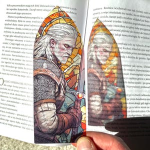 Może przedstawiać: Zakładka ze szkła witrażowego z szczegółową ilustracją mężczyzny z mieczem. Mężczyzna jest ubrany w kolczugę i skórzaną zbroję. Tło jest jaskrawo czerwone i pomarańczowe.