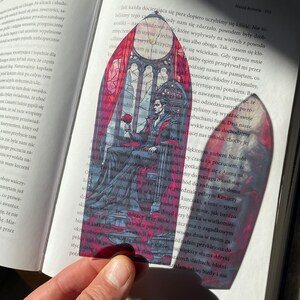 May include: A stained glass bookmark depicting a man in a black suit holding a red rose. The background is a gothic style window with red and black accents.