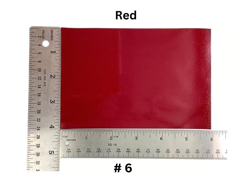 May include: A close-up of a red, rectangular piece of leather with a ruler measuring 6 inches in length. The leather is smooth and has a slight sheen. The ruler is marked with inches and picas. The text "#6" is printed below the ruler.