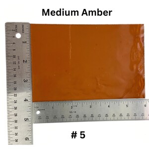 May include: A medium amber colored glass sheet measuring 5 inches by 6 inches. The sheet is sitting on top of a ruler.