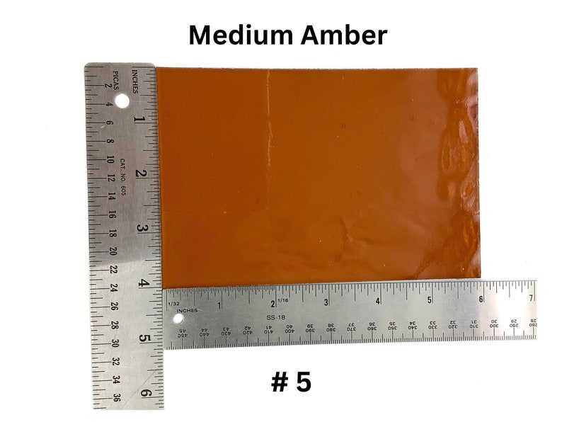 May include: A medium amber colored glass sheet measuring 5 inches by 6 inches. The sheet is sitting on top of a ruler.
