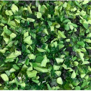 May include: Close-up of a pile of crushed glass pieces in various shades of green and black. The pieces are irregularly shaped and reflect light, creating a textured and vibrant appearance. The overall effect is a mix of light and dark green tones.