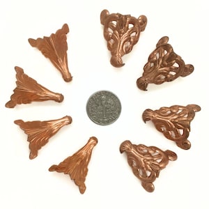 May include: Eight antique copper-colored furniture feet with a decorative floral design. The feet are arranged in a circle around a US dime for scale.