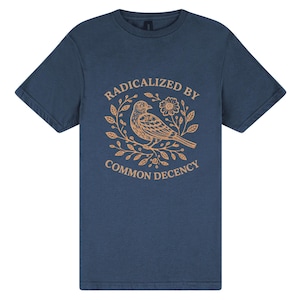 May include: A navy blue t-shirt with a tan graphic of a bird, flowers, and leaves. The text "RADICALIZED BY COMMON DECENCY" is arched above and below the bird illustration. The shirt has short sleeves and a crew neck.