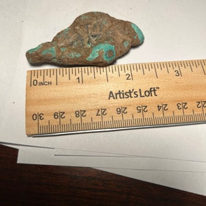 May include: A turquoise and brown rock with a rough texture. The rock is about 2 inches long and is next to a ruler.