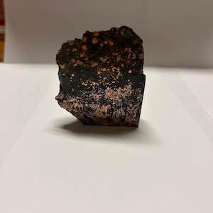 May include: A rough, dark gray rock with copper flecks and a smooth, polished surface.