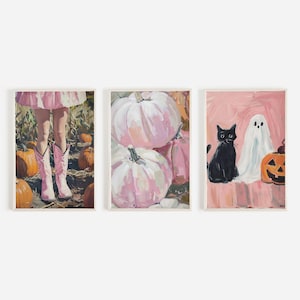 Puede incluir: Tres impresiones de arte enmarcadas con un tema de Halloween. La primera impresión muestra a una niña con botas rosas de pie en un campo de calabazas. La segunda impresión muestra un primer plano de calabazas rosas. La tercera impresión muestra un gato negro sentado junto a un fantasma y una calabaza de Halloween.
