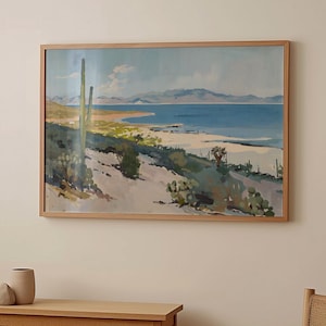 May include: A framed painting depicting a desert landscape with a large cactus in the foreground, a sandy beach, a body of water, and mountains in the distance. The painting is done in a watercolour style with shades of blue, green, and brown.