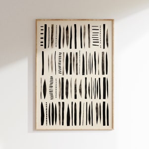 Op de afbeelding: Abstracte kunstprint in een houten lijst. Het kunstwerk toont een reeks zwarte verticale lijnen en vormen op een crèmekleurige achtergrond. De lijnen variëren in dikte en stijl, wat een minimalistische en moderne esthetiek creëert. De lijst is lichtbruin.