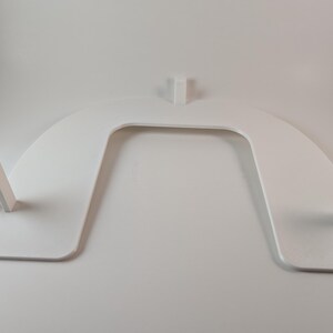 May include: A white, U-shaped object with a flat base and curved top. Two rectangular supports extend from the base, and a third support rises from the center of the top. The object appears to be made of a solid, smooth material.