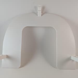 May include: A white, U-shaped, decorative shelf with a rectangular opening in the center. The shelf has a flat top and bottom with two small rectangular supports extending from the sides. A small rectangular piece extends from the top.