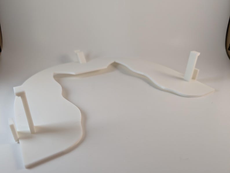 May include: A white, abstract, curved display stand with three vertical supports. The stand has a flowing, organic shape, and is made of a solid, opaque material. The design is minimalist and modern, suitable for showcasing items.