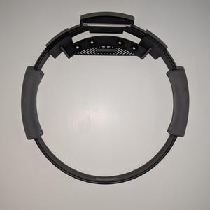 May include: A black exercise ring with gray foam padding on the inside of the ring. The ring has a black plastic piece on the top with a small silver button.