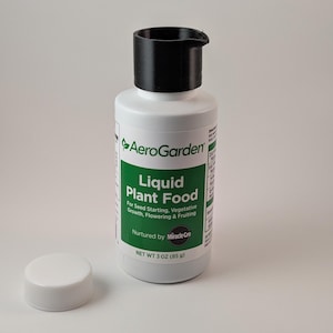 May include: A white plastic bottle with a black cap labelled "AeroGarden Liquid Plant Food" for seed starting, vegetative growth, flowering, and fruiting. The bottle is 3 ounces (85 g) and is nurtured by Miracle-Gro.