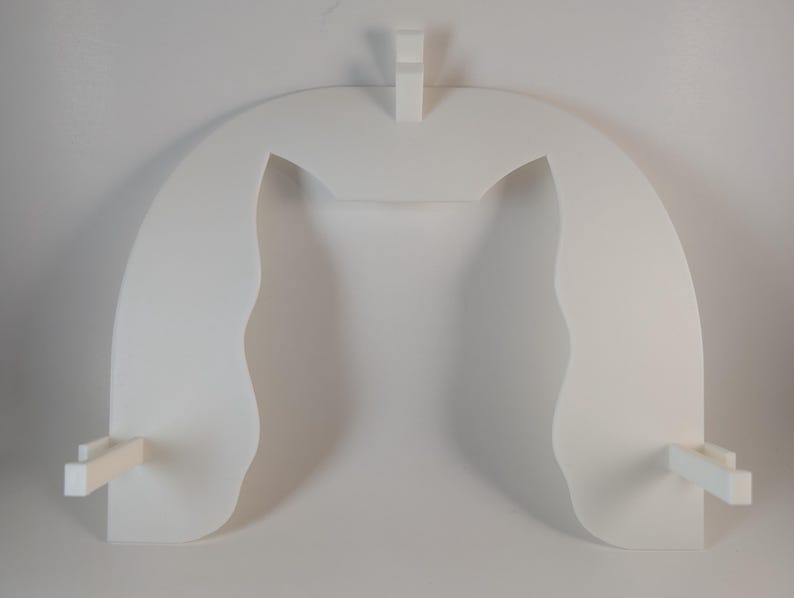 May include: A white, abstract wall shelf with a unique, arched design. The shelf features two curved side panels and a central support, with two small rectangular extensions at the base. The overall shape is reminiscent of a stylized architectural element.