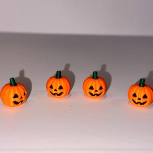 Può includere: Quattro piccole zucche di Halloween arancioni brillanti disposte in una fila orizzontale. Ogni zucca presenta un gambo verde scuro e un volto intagliato con occhi triangolari neri, un naso piccolo e una bocca dentellata e sorridente.