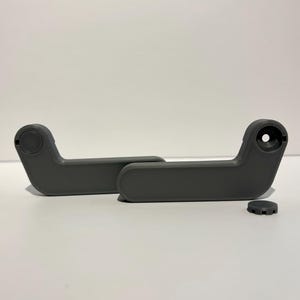 May include: Two gray plastic car seat handles with a matching small circular piece. The handles are curved with a rounded end and a hole on the other end. The small piece has a gear-like design.