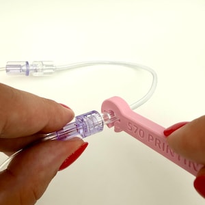 May include: A light pink plastic wrench tool with the text S70 PRINTING embossed on the side, being used to tighten a clear medical-grade luer lock connector attached to a thin, flexible, transparent plastic tube against a white background.