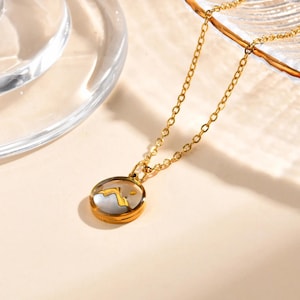 May include: A gold chain necklace with a round pendant featuring a white and gold mountain scene inside a clear glass dome.