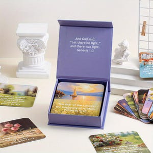 May include: A lilac box set of cards featuring Bible verses and landscape illustrations. The box is open, displaying cards with text including "The fear of the Lord is the beginning of wisdom." and "Genesis 1:3."