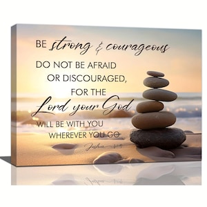 May include: A rectangular canvas wall art print featuring a stack of smooth, balanced stones on a sandy beach at sunset. The text reads: BE strong & courageous DO NOT BE AFRAID OR DISCOURAGED, FOR THE Lord your God WILL BE WITH YOU WHEREVER YOU GO Joshua 1:9.