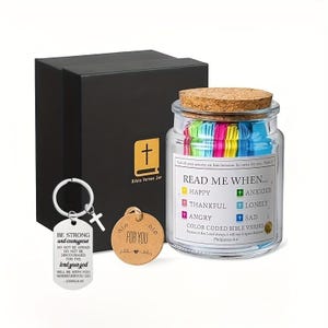 May include: A glass jar filled with colourful paper slips containing Bible verses. The jar has a cork lid and a label that reads "Read Me When..." with different emotions listed. The jar is accompanied by a small wooden tag that says "For You" and a keychain with a cross.