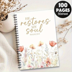 May include: A cream-coloured spiral-bound notebook with the text "He restores my soul" and Psalm 23:3 in gold lettering. The cover features a floral design with pink and orange flowers. The notebook has 100 pages. The cover also has a black circle with the text "100 pages".