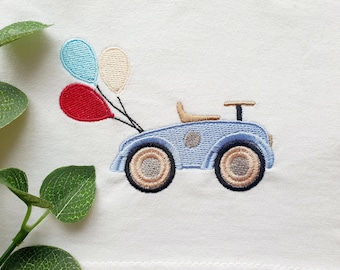 Pode incluir: Um carro de brinquedo azul com um volante castanho e rodas castanhas. O carro tem três balões presos à parte de trás, um vermelho, um azul claro e um creme.