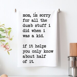 May include: White kitchen towel with black text that reads "mom, I'm sorry for all the dumb stuff I did when I was a kid. If it helps you only know about half of it." The towel is hanging on a silver bar.
