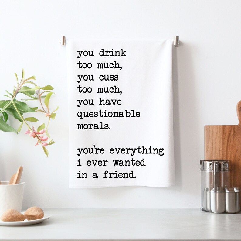 May include: White kitchen towel with black text that reads: "you drink too much, you cuss too much, you have questionable morals. You're everything I ever wanted in a friend." The towel is hanging on a silver bar.