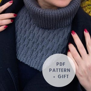 Puede incluir: Un calentador de cuello gris de punto con un patrón texturizado. El texto "PDF PATTERN + GIFT" está en un círculo blanco.