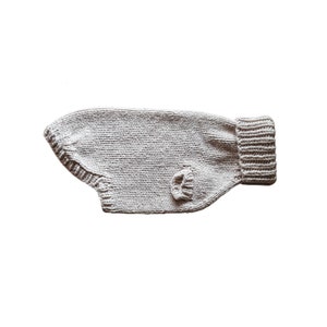 Pode incluir: Um suéter de tricô bege para cachorro com gola alta.