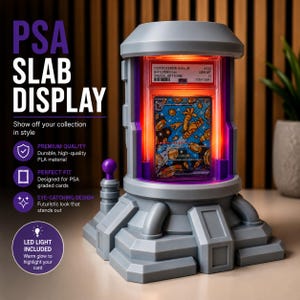 May include: A gray PSA slab display with a futuristic design, featuring a glowing interior that highlights a Pokemon card. The display includes the text "PSA SLAB DISPLAY" and "LED LIGHT INCLUDED".
