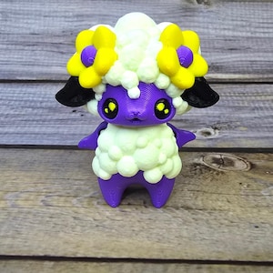 May include: A small, white, fluffy toy sheep with purple legs and a purple face. The sheep has yellow flowers on its head.