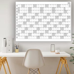 May include: A large white 2026 year wall calendar with a grid layout, displayed above a white desk. The calendar has a simple design with gray shaded blocks. A modern office setting with a white chair, desk accessories, and a potted plant.
