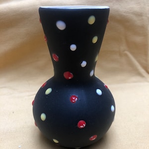 May include: A black ceramic vase with a round body and a narrow neck. The vase is decorated with white, yellow, and red polka dots.