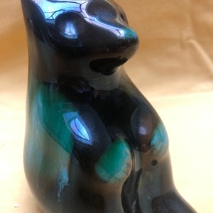 May include: A black and green ceramic figurine of a cat sitting with its paws tucked in. The cat has a glossy finish and a unique glaze pattern.