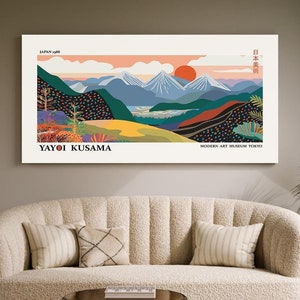 Könnte beinhalten: Ein farbenfrohes abstraktes Landschaftsbild mit einer Bergkette, einem See und einer roten Sonne. Das Bild ist gerahmt und hängt an einer Wand über einem weißen Sofa. Der Text "YAYOI KUSAMA" befindet sich am unteren Rand des Bildes.