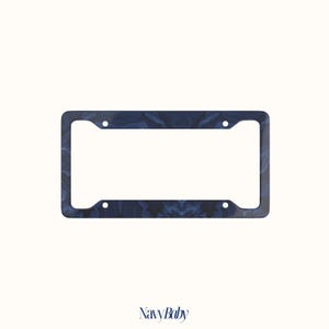 May include: A rectangular license plate frame featuring a dark navy blue and black marbled pattern with a smooth finish. The frame includes four circular mounting holes positioned at the corners to secure it to a vehicle. The text NavyBaby is below.