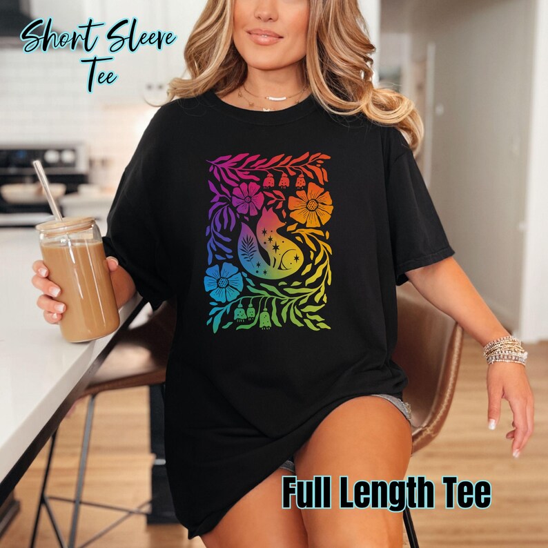 May include: Black short sleeve tee featuring a colourful, rainbow-hued floral and fox design. The graphic includes flowers, leaves, and a crescent moon. Text on the shirt reads "Short Sleeve Tee" and "Full Length Tee".
