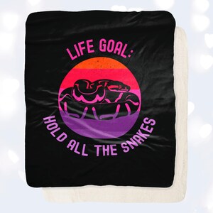 May include: Black and white throw blanket with a pink, purple, and red circle graphic. The circle graphic features a snake and the text "Life Goal: Hold All The Snakes".