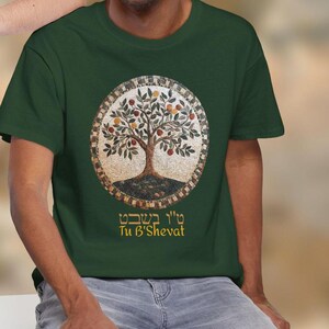 May include: Dark green t-shirt featuring a circular design with a tree illustration. The tree has brown branches, green leaves, and orange fruit. The text "Tu B'Shevat" is below the tree design.
