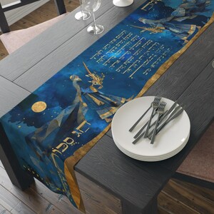 May include: A blue and gold table runner with Hebrew text and illustrations of figures. The runner has a dark blue background with gold accents and a celestial design. The runner is on a dark wooden table.