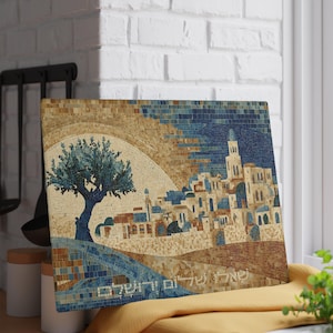 May include: A mosaic art piece showing a cityscape with a tree and buildings. The artwork uses blues, browns, and beige. The image includes Hebrew text. The art piece is displayed on a window sill.