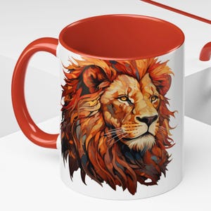 Może przedstawiać: Biały ceramiczny kubek z czerwonym wnętrzem i uchwytem. Kubek przedstawia szczegółową ilustrację głowy lwa z żywą grzywą w odcieniach pomarańczu, brązu i żółci. Kubek jest przeznaczony do gorących napojów.