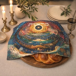 May include: A square fabric challah cover featuring a colorful, detailed illustration of the creation story with Hebrew text and the English phrase In the beginning God created, draped over a braided loaf of bread on a round wooden board.
